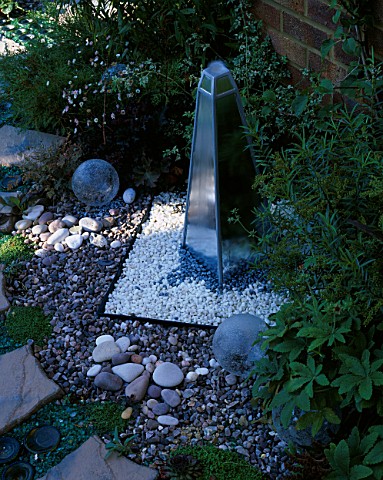 MIRRORED_OBELISK_WATERFEATURE_SURROUNDED_BY_RECYCLED_GLASS_BOTTLES_AND_CIRCULAR_PAVED_AREA_DESIGNER_