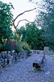 LA CHABAUDE  FRANCE. DESIGNER - PHILIPPE COTTET: GRAVEL TERRACE WITH LARGE WOODEN LOG SEAT  STONE WALL AND DEAD TREE SCULPTURE