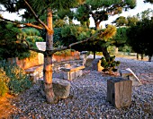LA CHABAUDE  FRANCE.DESIGNER - PHILIPPE COTTET: STONE AND WOOD SEATING AREA ON GRAVEL TERRACE WITH PINE TREE
