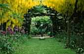 THE ABBEY HOUSE  WILTSHIRE: THE LABURNUM ARCH IN SPRING WITH ALLIUMS AND MOTHER AND CHILD SCULPTURE BY BOB ALLEN