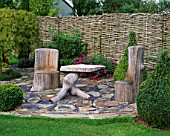 WOODEN SEATS  AND TABLE ON SLATE TERRACE WITH BOX TOPIARY SHAPES AND WILLOW FENCE. DESIGNER: JOHN MASSEY