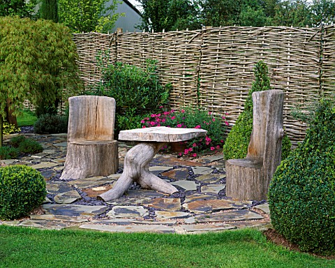 WOODEN_SEATS__AND_TABLE_ON_SLATE_TERRACE_WITH_BOX_TOPIARY_SHAPES_AND_WILLOW_FENCE_DESIGNER_JOHN_MASS