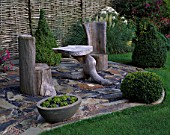 WOODEN SEATS AND TABLE ON SLATE TERRACE WITH TOPIARY BOX SHAPES AND WILLOW FENCING. DESIGNER: JOHN MASSEY