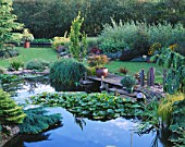 VIEW ACROSS THE LILY POND TO WOODEN PONTOON WITH STANDING STONES. DESIGNER : JOHN MASSEY
