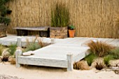 WOODEN CONTAINERS ON DECKING IN SEASIDE GARDEN PLANTED WITH PINES AND GRASSES: DESIGNERS NIGEL DUFF AND GREG RIDDLE. BEACH BOARDWALK  WOODEN SEAT
