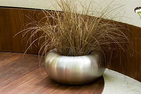 SPUN_STAINLESS_STEEL_CONTAINER_ON_WOODEN_DECK_PLANTED_WITH_CAREX_BUCHANANII_CONTAINER_DESIGNED_BY_MA
