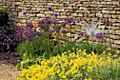 A DELICATE GLASS SCULPTURE BY NEIL WILKIN BESIDE A STONE WALL AND BORDER PLANTED WITH ALLIUMS AND HELIANTHEMUMS. WINGWELL NURSERY   RUTLAND
