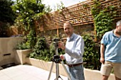 CLIVE NICHOLS WITH TRIPOD IN  CONTEMPORARY CLASSIC GARDEN DESIGNED BY CHARLOTTE ROWE