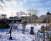 WINTER  WOODCHIPPINGS  NORTHAMPTONSHIRE: THE GARDEN IN SNOW WITH A STATUE IN THE FOREGROUND AND THE HOUSE BEHIND