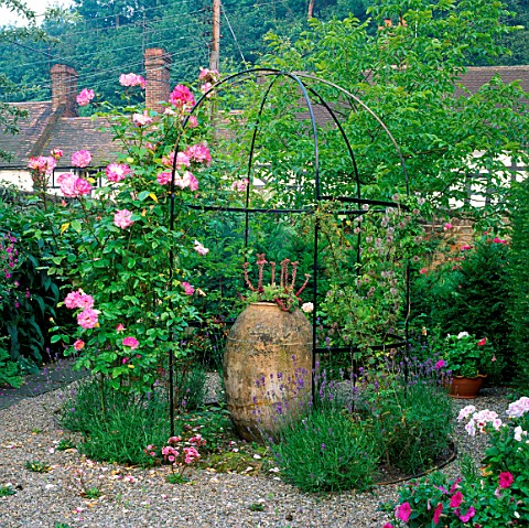 METAL_ARBOUR_WITH_CLIMBING_ROSE_HANDEL_SURROUNDS_AN_OLD_EGYPTIAN_VASE_PLANTED_WITH_SEMPERVIVUM_LOWER