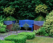 RIDLERS GARDEN  SWANSEA  WALES: BLUE BENCH WITH LEAD AND RUSTY METAL CONTAINERS BESIDE PLANTED WITH HOLLY AND BOX
