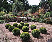 MAYROYD MILL HOUSE  YORKSHIRE: DESIGNERS: RICHARD EASTON AND STEVE MACKAY - BOX BALLS IN GRAVEL WITH WOODEN TABLE & CHAIRS ON PATIO AREA AND HERBACEOUS PERENNIAL BORDERS