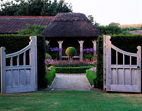 DOUBLE_GATES_OPEN_TO_VIEW_ACROSS__FORMAL_TOPIARY_GARDEN_TO_THATCHED_SUMMER_HOUSE_AT_LADY_FARM__SOMER