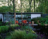 CHELSEA 2005: MERRILL  LYNCH GARDEN DESIGNED BY ANDY STURGEON: GLASS FRONTED OFFICE WITH POOL AND NATURALISTIC PLANTING OF STIPA TENUISSIMA  IRISES  CARDOONS AND SALVIAS