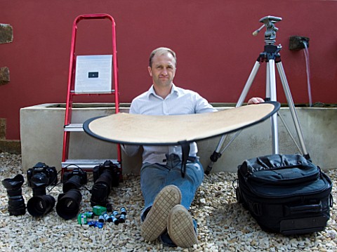 CLIVE_NICHOLS_HOLDING_A_REFLECTOR_IN_HIS_GARDEN_WITH_CAMERA_EQUIPMENT