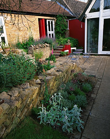 WINGWELL_NURSERY__RUTLAND_VIEW_TO_THE_BACK_OF_THE_HOUSE_WITH_RED_WALL__METAL_TABLE_AND_CHAIRS_PATIO