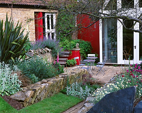 WINGWELL_NURSERY__RUTLAND_VIEW_TO_THE_BACK_OF_THE_HOUSE_WITH_RED_WALL__STACHYS__PHORMIUM___METAL_TAB