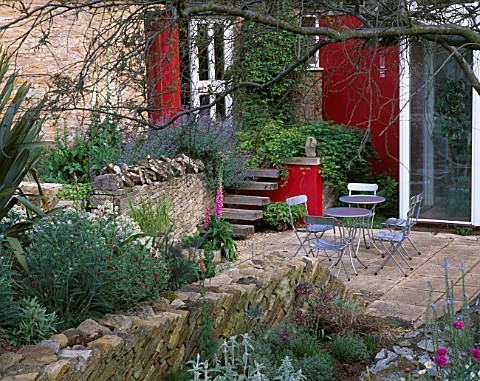 WINGWELL_NURSERY__RUTLAND_VIEW_TO_THE_BACK_OF_THE_HOUSE_WITH_RED_WALL__STACHYS__PHORMIUM___METAL_TAB