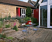 WINGWELL NURSERY  RUTLAND: VIEW TO THE BACK OF THE HOUSE WITH RED WALL  METAL TABLE AND CHAIRS. PATIO