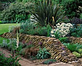 WINGWELL NURSERY  RUTLAND: WALL AT THE BACK OF THE HOUSE WITH CRAMBE MARITIMA  PHORMIUM  STACHYS  ALLIUMS AND POTENTILLAS