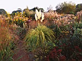 AUTUMN BORDER OF MIXED GRASSES AND PERENNIALS BESIDE BRICK PATH AT MARCHANTS HARDY PLANTS  EAST SUSSEX