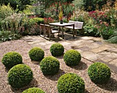MAYROYD MILL HOUSE  YORKSHIRE: DESIGNERS: RICHARD EASTON AND STEVE MACKAY - GRAVEL TERRACE WITH BOX BALLS  WOODEN TABLE AND CHAIRS ON PATIO AND HERBACEOUS PERENNIAL BORDER