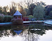 GARDEN DESIGNED BY DUNCAN HEATHER: THE SUMMERHOUSE AND WOODEN BRIDGE ACROSS THE POOL IN WINTER WITH CORNUS AND TREE REFLECTIONS IN THE WATER