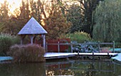GARDEN DESIGNED BY DUNCAN HEATHER: THE SUMMERHOUSE AND WOODEN BRIDGE ACROSS THE POOL IN WINTER WITH CORNUS AND TREE REFLECTIONS IN THE WATER