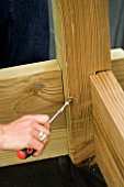 CLARE MATTHEWS SCREWS A SCREW INTO A WOODEN CORNER SUPPORT OF THE BEDS IN THE POTAGER. DESIGNER: CLARE MATTHEWS