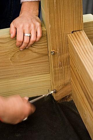 CLARE_MATTHEWS_SCREWS_A_SCREW_INTO_A_WOODEN_CORNER_SUPPORT_OF_THE_BEDS_IN_THE_POTAGER_DESIGNER_CLARE