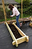 CLARE MATTHEWS DIGGING COMPOST INTO A WOODEN BED IN THE POTAGER