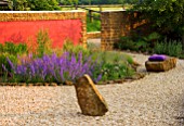 RICKYARD BARN GARDEN  NORTHAMPTONSHIRE: VIEW ACROSS GRAVEL GARDEN TO ROCK  RED WALL  NEPETA WALKERS LOW AND ROCK SEAT WITH PURPLE CUSHION