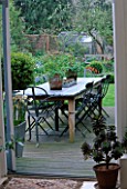 LISETTE PLEASANCE GARDEN  LONDON: VIEW OUT OF CONSERVATORY TO DECKED TERRACE WITH LEAD TABLE AND CHAIRS