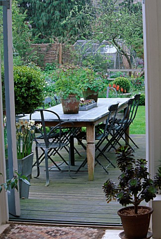 LISETTE_PLEASANCE_GARDEN__LONDON_VIEW_OUT_OF_CONSERVATORY_TO_DECKED_TERRACE_WITH_LEAD_TABLE_AND_CHAI