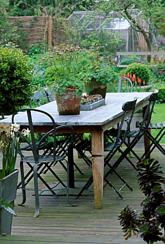 LISETTE_PLEASANCE_GARDEN__LONDON_VIEW_OUT_OF_CONSERVATORY_TO_DECKED_TERRACE_WITH_LEAD_TABLE_AND_CHAI