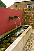 RICKYARD BARN  NORTHAMPTONSHIRE: THE GRAVEL COURTYARD IN JUNE WITH RED WALL  WATER SPOUTS AND TROUGH ( WATER FEATURE)