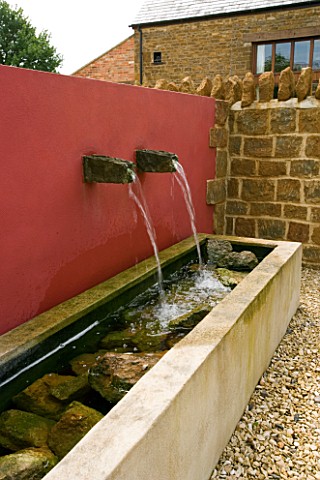 RICKYARD_BARN__NORTHAMPTONSHIRE_THE_GRAVEL_COURTYARD_IN_JUNE_WITH_RED_WALL__WATER_SPOUTS_AND_TROUGH_