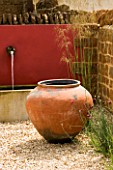 RICKYARD BARN  NORTHAMPTONSHIRE: THE GRAVEL COURTYARD IN JUNE WITH LARGE TERRACOTTA CONTAINER  RED WALL  WATER SPOUTS AND TROUGH