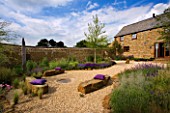 RICKYARD BARN GARDEN  NORTHAMPTONSHIRE: THE GRAVEL GARDEN WITH ROCKS AND BORDERS OF GRASSES AND PERENNIALS WITH THE HOUSE TO THE RIGHT