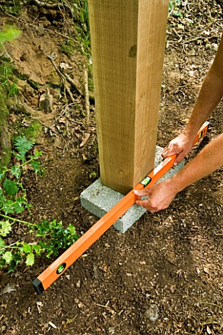 DESIGNER_CLARE_MATTHEWS_TREEHOUSE_PROJECT_USING_A_SPIRIT_LEVEL_TO_CHECK_THAT_CONCRETE_BLOCK_IS_LEVEL
