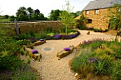 RICKYARD BARN GARDEN  NORTHAMPTONSHIRE: VIEW OVER THE GRAVEL GARDEN WITH ROCK SEATS  CUSHIONS  THE HOUSE AND DRIFTWOOD SCULPTURE