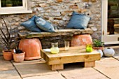 DESIGNER: CLARE MATTHEWS - LOW SLEEPER TABLE PROJECT: WOODEN SEAT WITH BLUE CUSHIONS IN FRONT OF LOW SLEEPER TABLE ON PATIO