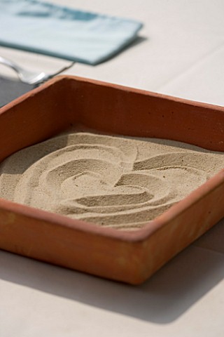DESIGNER_CLARE_MATTHEWS__ZEN_TRAY_SQUARE_TERRACOTTA_DISH_ON_TABLE_WITH_SAND_MADE_INTO_A_HEART_SHAPE