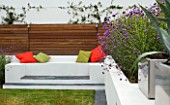 MINIMALIST GARDEN DESIGNED BY WYNNIATT-HUSEY CLARKE: RENDERED WHITE WALL WITH SEAT AND ORANGE CUSHIONS  VERBENA BONARIENSIS AND MISCANTHUS ZEBRINUS  AGAVE AMERICANA IN CONTAINER