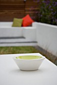 MINIMALIST GARDEN DESIGNED BY WYNNIATT-HUSEY CLARKE: SIMPLE BOWL WITH GREEN INSIDE ON WHITE METAL TABLE WITH ORNAGE AND LIME GREEN CUSHIONS BEHIND