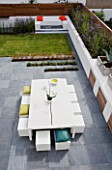 MINIMALIST GARDEN DESIGNED BY WYNNIATT-HUSEY CLARKE: VIEW ONTO GREY SLATE PATIO WITH WHITE METAL TABLE AND CHAIRS  WHITE RENDERED WALLS  SEAT WITH ORANGE CUSHIONS