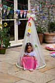 DESIGNER CLARE MATTHEWS: CHILDRENS PARTY - GIRL SITTING IN COCOON ON PATIO WITH BUNTING BEHIND