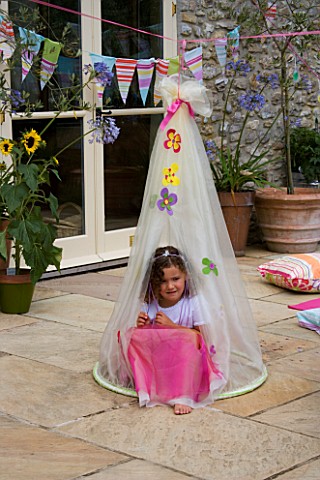 DESIGNER_CLARE_MATTHEWS_CHILDRENS_PARTY__GIRL_SITTING_IN_COCOON_ON_PATIO_WITH_BUNTING_BEHIND