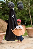 DESIGNER CLARE MATTHEWS: CHILDRENS PARTY - BOY ON PATIO DRESSED AS A PIRATE AND IN A PAPER SHIP BESIDE BLACK PIRATE TENT