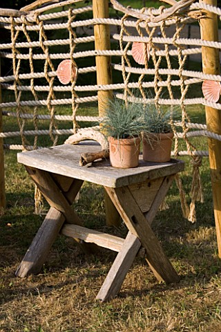 DESIGNER_CLARE_MATTHEWS_ROPE_SCREEN_HIDEAWAY__WOODEN_TABLE_WITH_TERRACOTTA_CONTAINERS_AND_DRIFTWOOD_